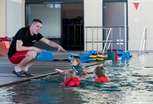 Schwimmmeister zeigt Kindern Schwimmbewegungen. 