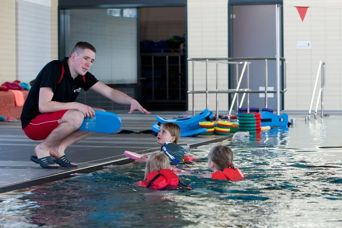 Schwimmmeister zeigt Kindern Schwimmbewegungen. 