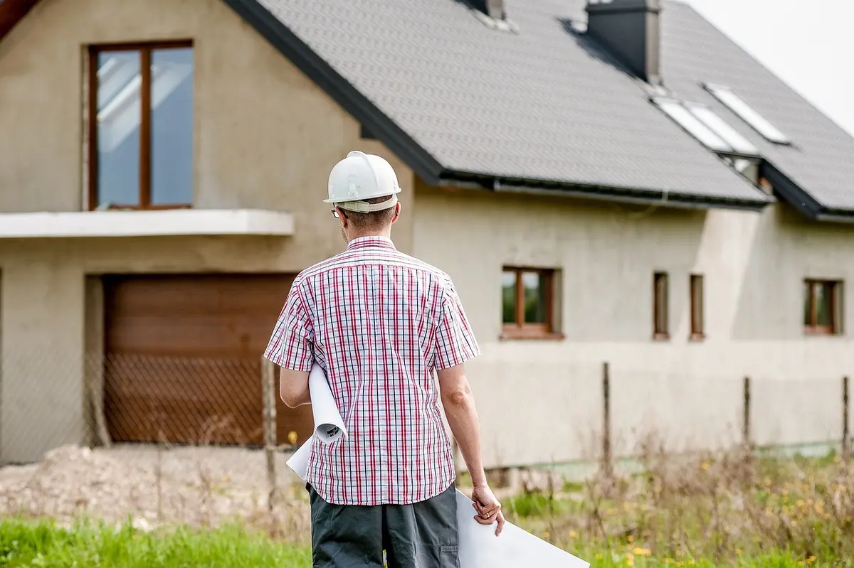 Ein Mann mit Bauarbeiterhelm steh vor einem Haus.