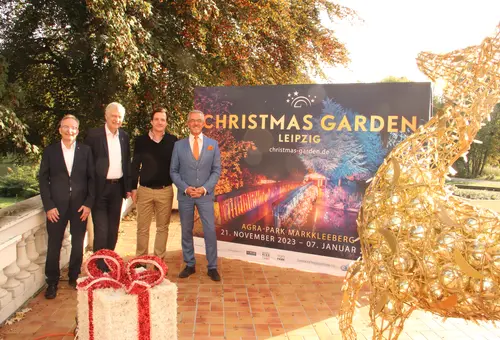 Vier Männer stehen vor einer Plakatwand, die einen Eindruck verschaffen sollen, wie ab 21. November die Lichtinstallationen im Park aussehen werden.
