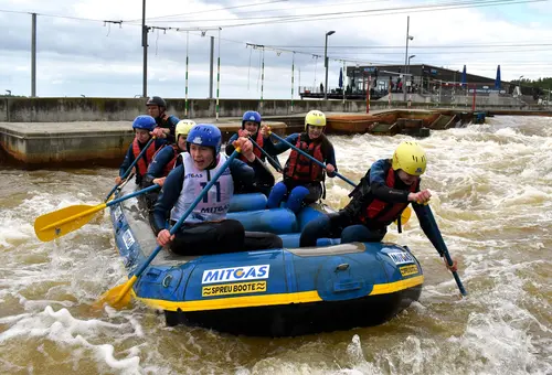 Schülerinnen und Schüler kämpfen sich in einem Raftingboot durch den Wildwasserkanal.