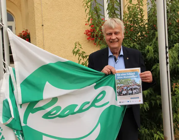 Oberbürgermeister Karsten Schütze hält die Flagge der "Mayors for Peace" so, dass der Schriftzug "Peace" zu sehen ist.