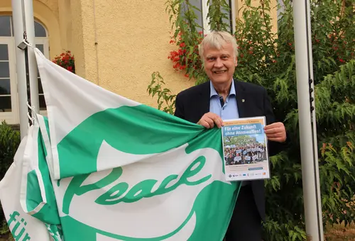Oberbürgermeister Karsten Schütze hält die Flagge der "Mayors for Peace" so, dass der Schriftzug "Peace" zu sehen ist.